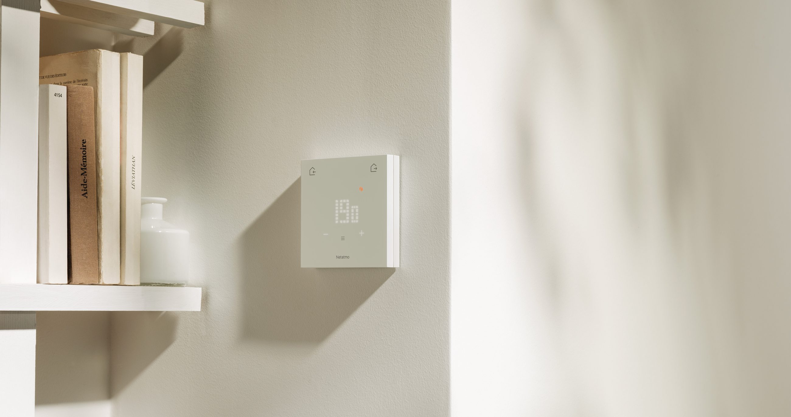 Le Thermostat ORIGINAL fixé sur un mur clair, à côté d'une étagère de livres